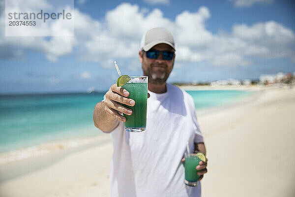 Glücklicher Millennial-Mann hält tropisches Getränk am karibischen Strand hin