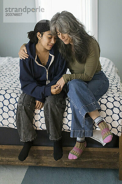 Weiße Mutter umarmt ihre gemischtrassige Teenager-Tochter im Schlafzimmer