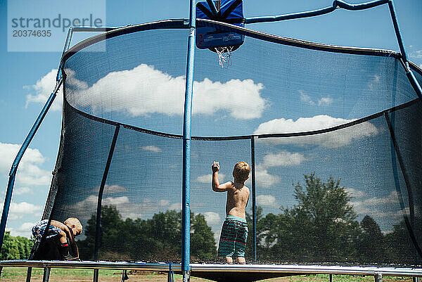Weite Sicht auf zwei Jungen  die draußen mit Wolken auf einem Trampolin springen