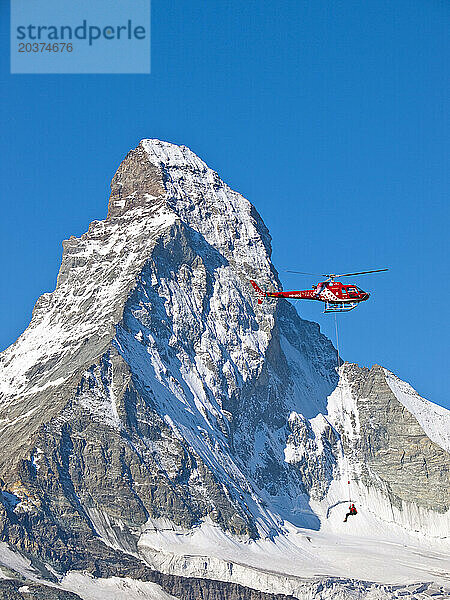 Ein Rettungseinsatz schwebt unter einem Helikopter der Air Zermatt in den Schweizer Alpen  im Hintergrund die Nordwand des berühmten Matterhorns.