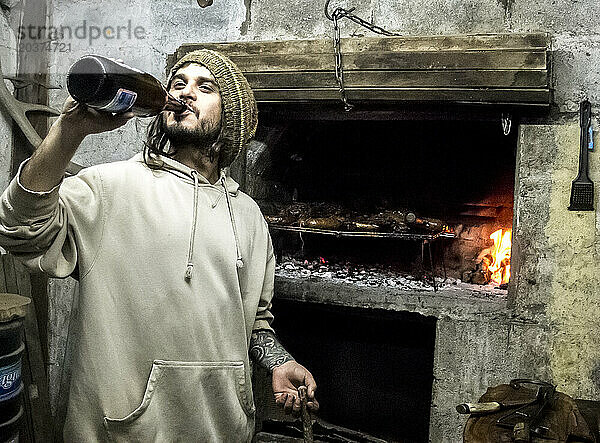 Ein Mann trinkt ein Bier  während er in Bariloche  Argentinien  ein Asado kocht