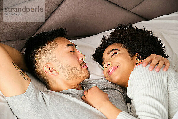 Multiethnisches Paar schaut sich im Bett liebevoll an.