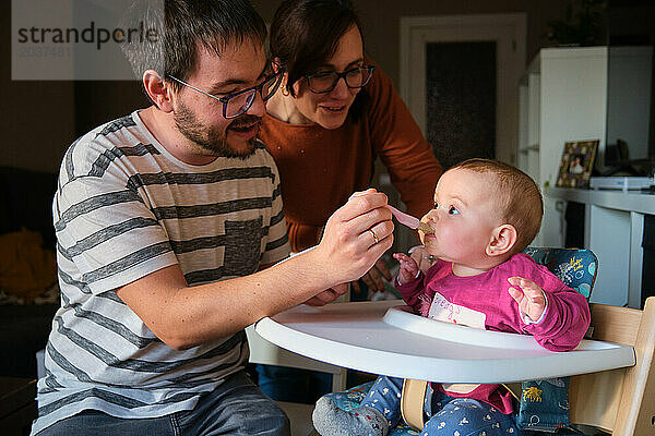 Eltern füttern ihr 6 Monate altes Mädchen mit Babynahrung  Fruchtpüree.