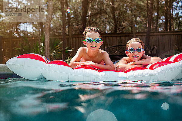 Fröhliche Kinder grinsen auf einem gestreiften Schwimmkörper in einem schimmernden Pool