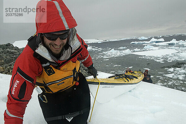 Ein Mann schleppt ein Kajak eine steile Eisböschung an der Westküste der antarktischen Halbinsel namens Graham Land hinauf.