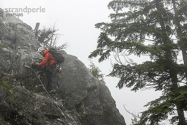 Ein Mann bewegt sein Seil zum nächsten Kabel  während er die Via Ferrata in Squamish  British Columbia  erklimmt.