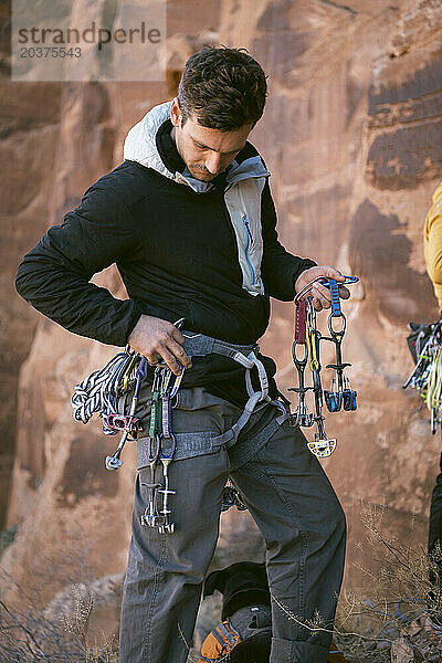 Männlicher Bergsteiger mit Kletterausrüstung steht an einer Klippe in der Wüste