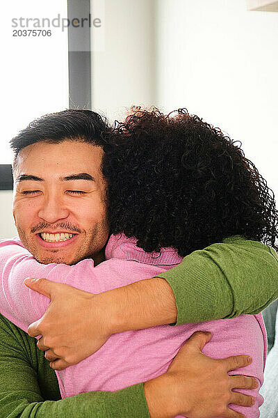Asiatischer Mann umarmt seine lateinamerikanische Freundin zu Hause.