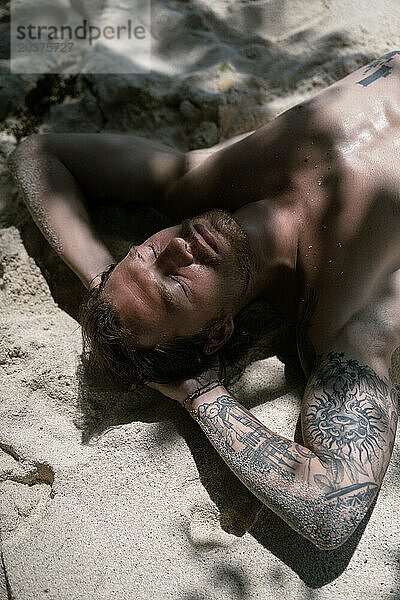 Mann mit Tätowierungen entspannt sich im Urlaub am Sandstrand. Nusa Lembongan