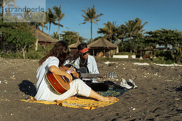 Freundinnen spielen Gitarren am Strand. Sonnenuntergang am Meer. Bali