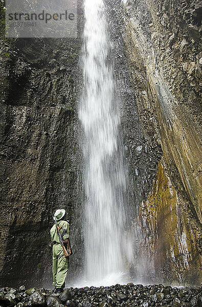 Ein bewaffneter Parkwächter und Führer steht in der Nähe eines Wasserfalls im Arusha-Nationalpark  Tansania.