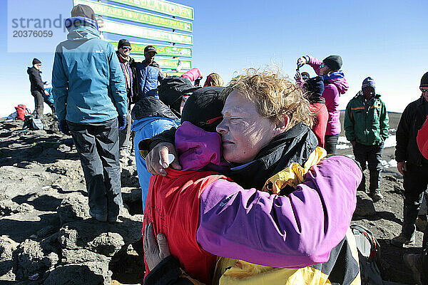 Zwei Wanderinnen weinen vor Glück und umarmen sich auf dem Gipfel des Kilimandscharo.