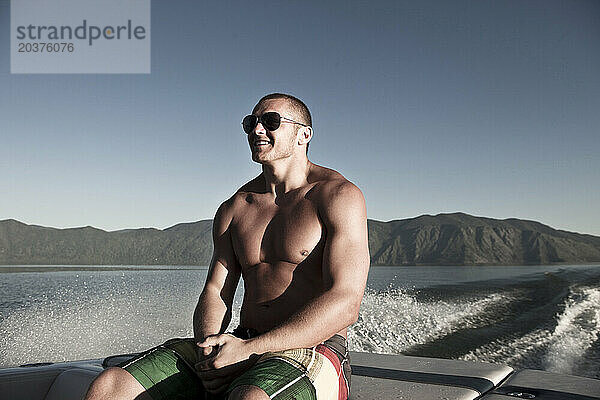 Ein sportlicher Mann lächelt  während er auf dem Heck eines Wakeboard-Bootes in Idaho fährt.