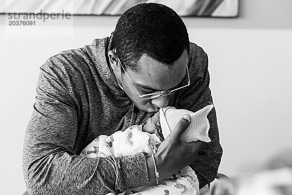 Afroamerikanischer Vater hält und küsst neugeborenes Baby zum ersten Mal