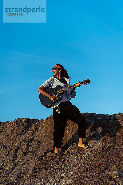 Musikerin singt und spielt Gitarre am Strand. In einem Bandana. Bali