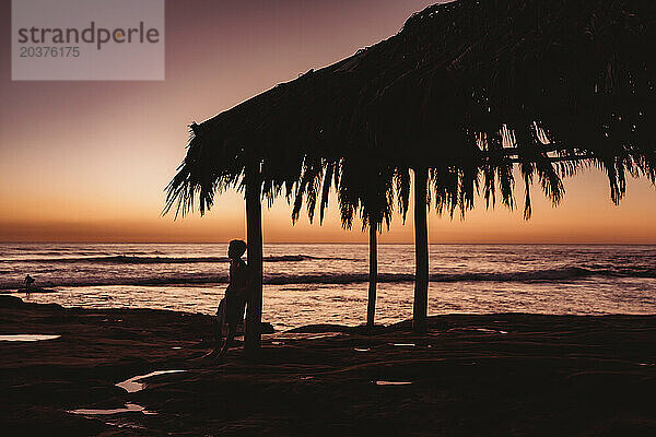 Silhouette eines Jungen mit dem Meer und Sonnenuntergang im Hintergrund