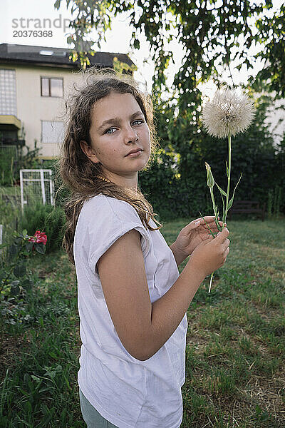 Teenager-Mädchen mit einer Löwenzahnblume in ihren Händen im Sommergarten