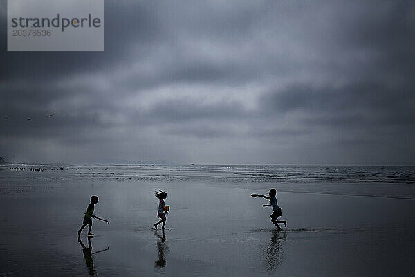 Drei Kinder spielen an einem bewölkten Tag am Meer