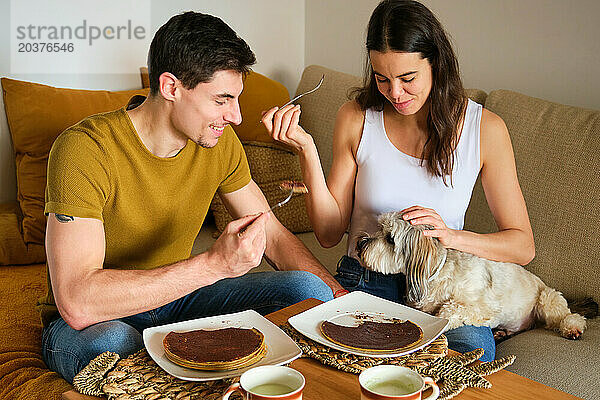 Spanisches Paar isst zu Hause Pfannkuchen mit seinem Hund.