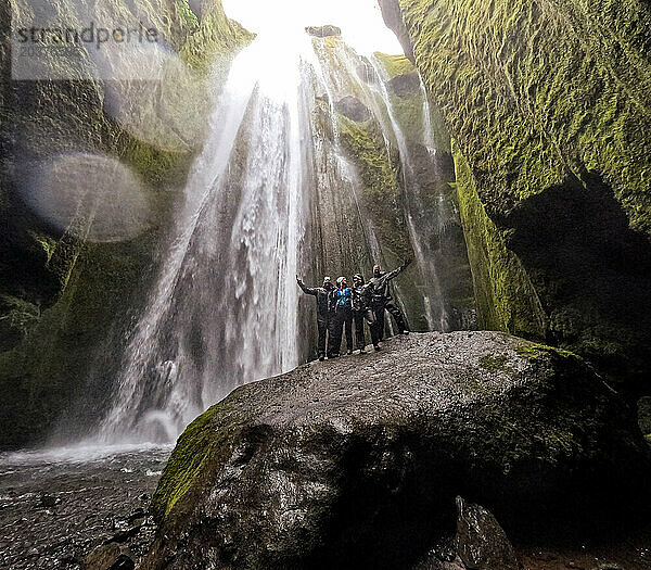 Gruppe Erwachsener auf riesigem Felsen mit Wasserfall  der die Klippen hinunterstürzt