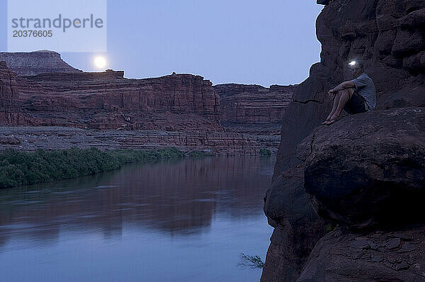 Ein Mann beobachtet  wie ein Mond über einem Fluss aufgeht.