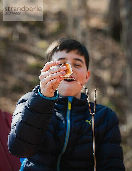 Fröhlicher Junge  der an einem Frühlingstag draußen einen Marshmallow anstößt.