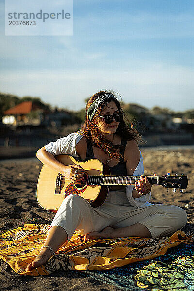 Musikerin singt und spielt Gitarre am Strand. In einem Bandana. Bali