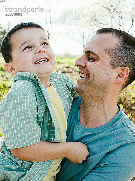 Lachender und lächelnder Vater  der seinen Sohn im Frühling zusammenhält