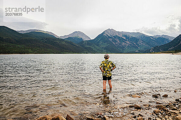 Junge in einem farbenfrohen Hemd steht an einem ruhigen Bergsee