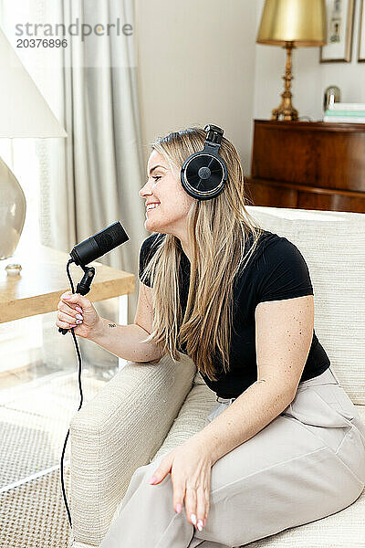 Glückliche Frau mit Mikrofon und Kopfhörern  die einen Podcast aufnimmt