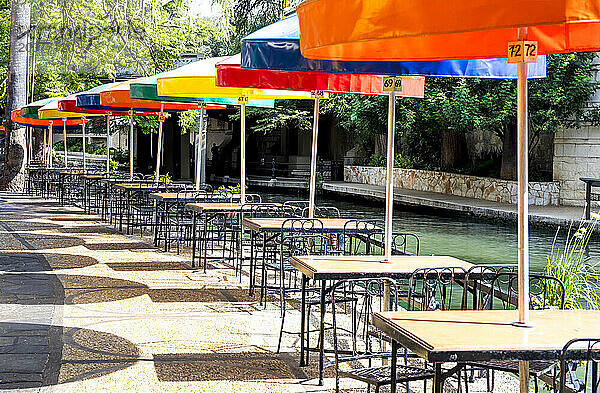 An einem sonnigen Spätsommertag decken bunte Sonnenschirme die Tische in einem Restaurant am San Antonio River Walk ab.