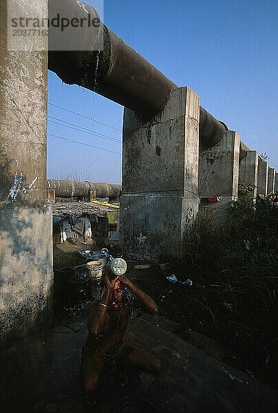 Bewohner eines Slums in Delhi  Indien  die unterhalb der Leitung leben  die Wasser in die Stadt bringt. Diese Menschen verfügen über Handpumpen  mit denen sie Grundwasser zum Baden und Trinken gewinnen.