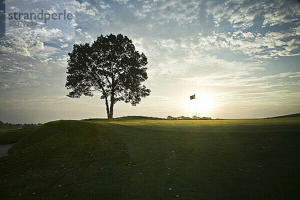 Die aufgehende Sonne erzeugt die Silhouette der Flagge eines Putting Greens.