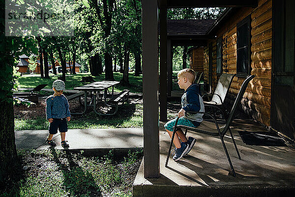 Seitenansicht von zwei Jungen zusammen vor einer Hütte im Wald im Sommer