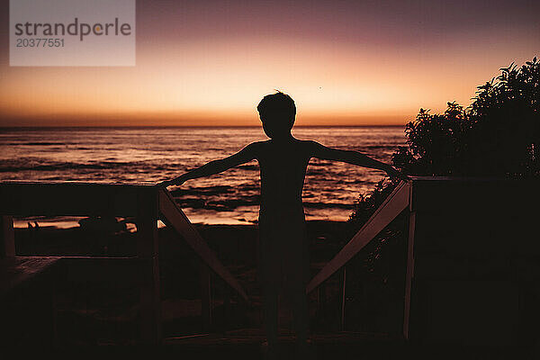 Silhouette eines Jungen mit dem Meer und Sonnenuntergang im Hintergrund