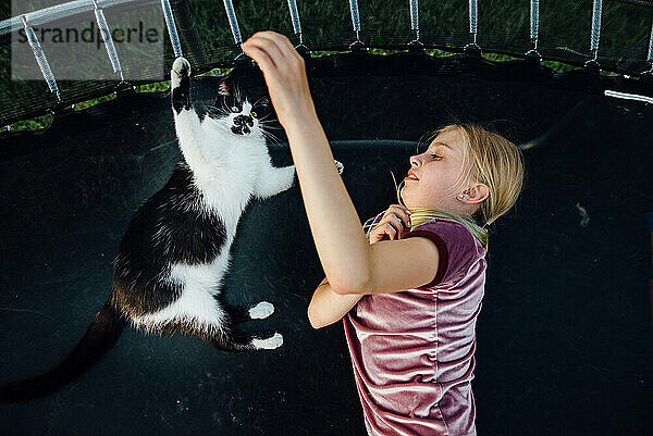 Blick von oben auf ein Mädchen  das im Sommer mit einer Katze auf dem Trampolin spielt.