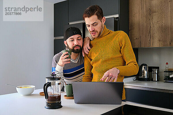 Homosexuelles Paar benutzt den Laptop und redet beim Frühstück.