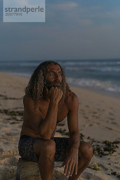 Porträt eines glücklichen Mannes mit langen lockigen Haaren bei Sonnenuntergang am Strand.