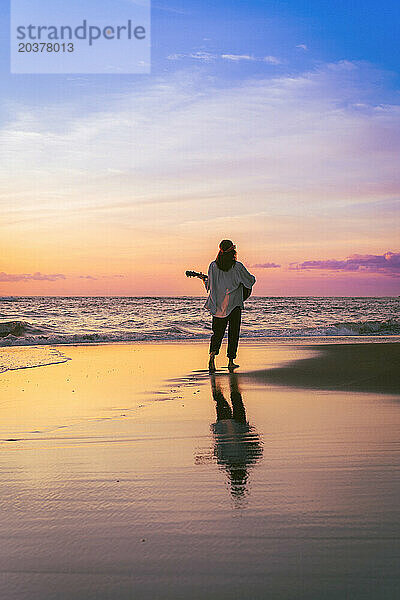 Musikerin mit Gitarre am Strand bei Sonnenuntergang. Bali