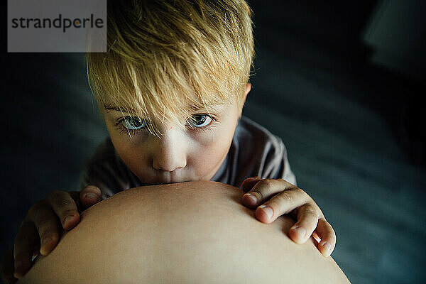Porträt eines kleinen Jungen  der drinnen den schwangeren Babybauch einer Mutter küsst
