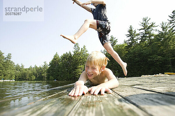 Ein Kind springt von einem Holzfloß in Center Harbor  New Hampshire  über ein anderes Kind in einen See.