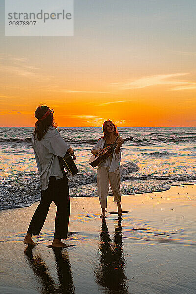 Freundinnen spielen Gitarren am Strand. Sonnenuntergang am Meer. Bali