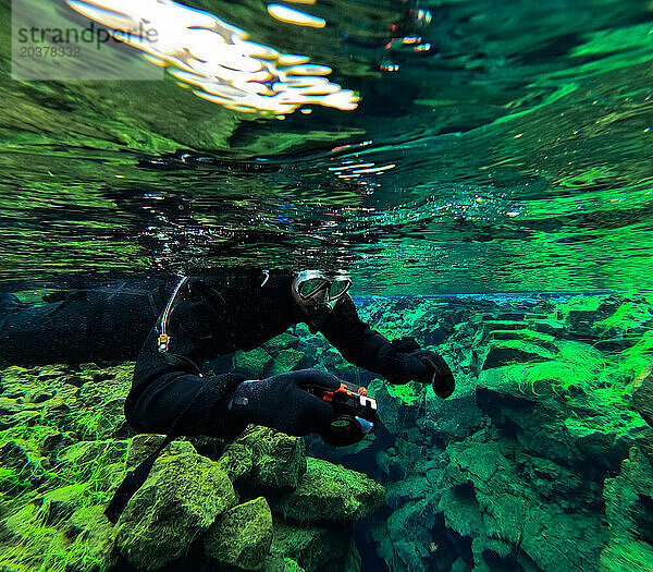 Mann schwimmt und fotografiert unter Gletscherwasser mit Grünalgen