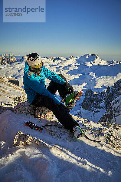 Alpinist zieht nach einem Winteraufstieg seine Steigeisen aus.