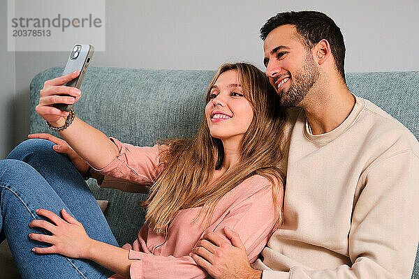 Spanisches glückliches Paar macht gemeinsam ein Selfie auf einem Sofa zu Hause.