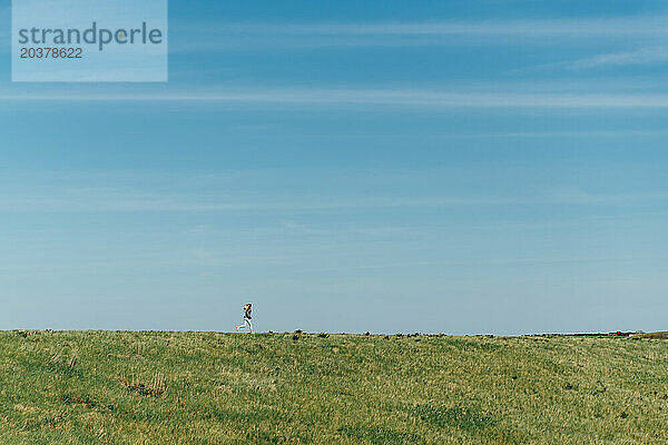 Sehr weite Sicht auf ein Mädchen  das am Gipfel eines Hügels mit blauem Himmel läuft.