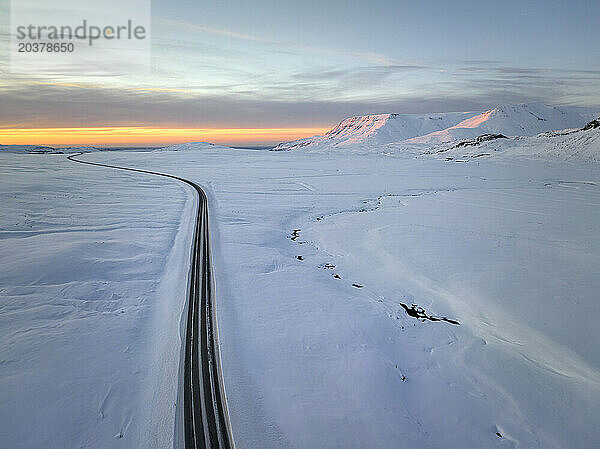 Lange Asphaltstraße in schneebedecktem Gelände