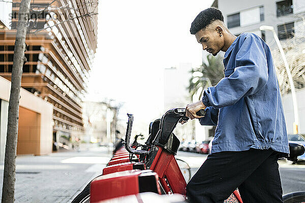 Junger erwachsener Mann hält ein rotes Fahrrad auf der Straße.