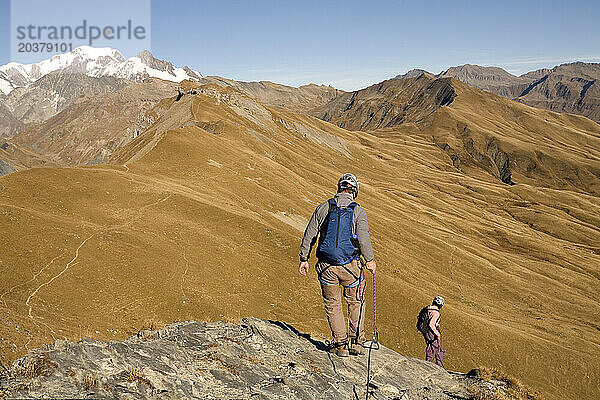 Zwei Personen steigen eine Klippe hinab  während sie in den französischen Alpen den Klettersteigsport ausüben.