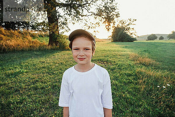 Fröhlicher Junge lächelt auf der Wiese und trägt ein weißes T-Shirt
